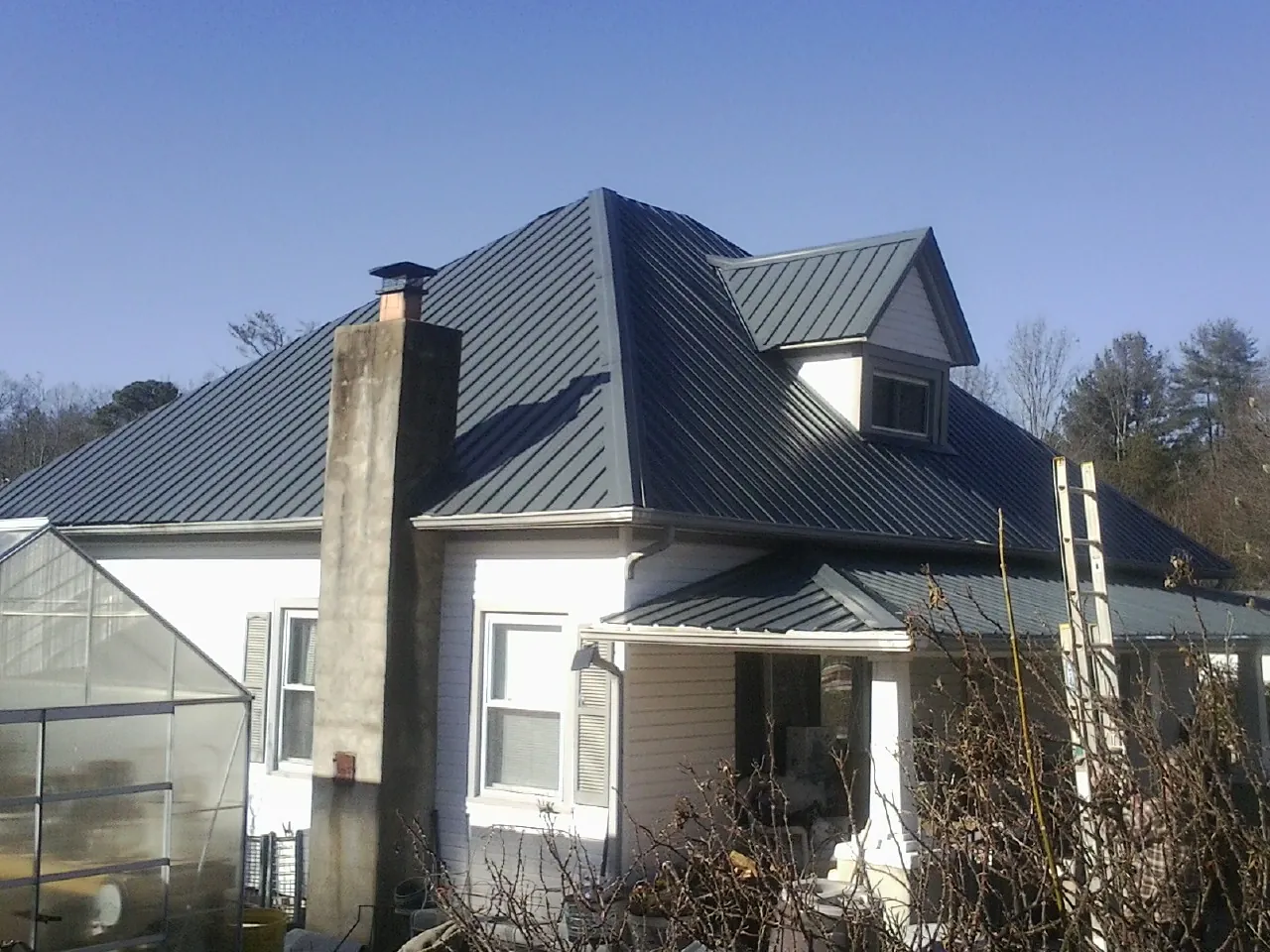 Dark blue standing seam metal roof on a white farmhouse with dormer — Slate & Tile Roof Repair by Roofing Brothers in Goose Lake