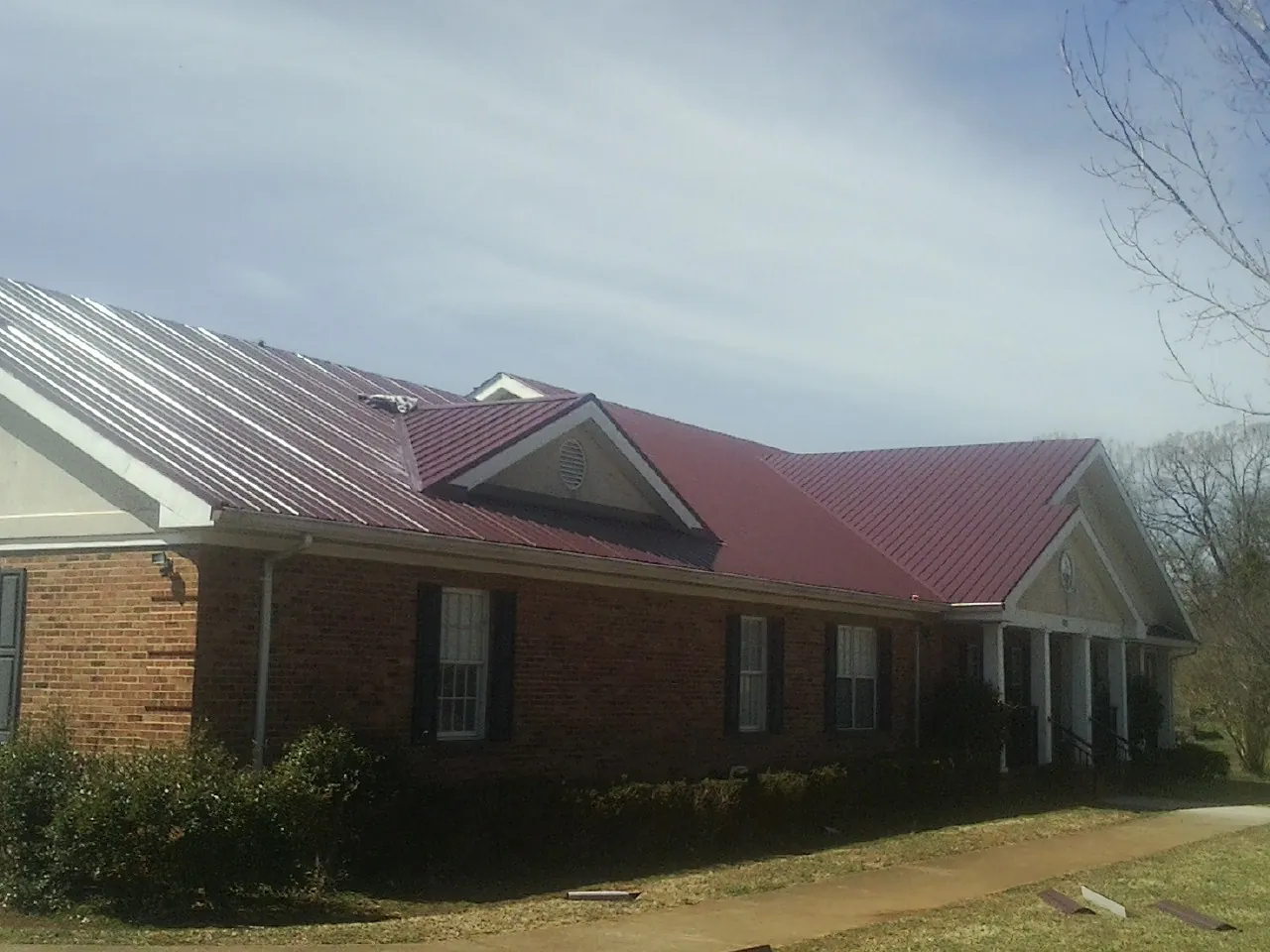 Red metal roof with gabled entries on a long brick building, from a Hail Damage Roof Repair job in Goose Lake