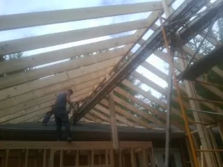 Rafters going up over a new addition with a worker on the wall in Goose Lake