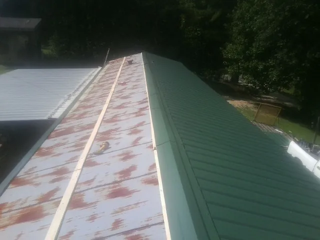 Old rusted panels beside newly installed green metal roofing — Wind Damage Roof Repair by Roofing Brothers in Goose Lake
