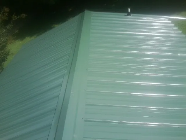 New green metal panels meeting at the ridge of a roof — Flat Roof Repair work by our crew in Goose Lake