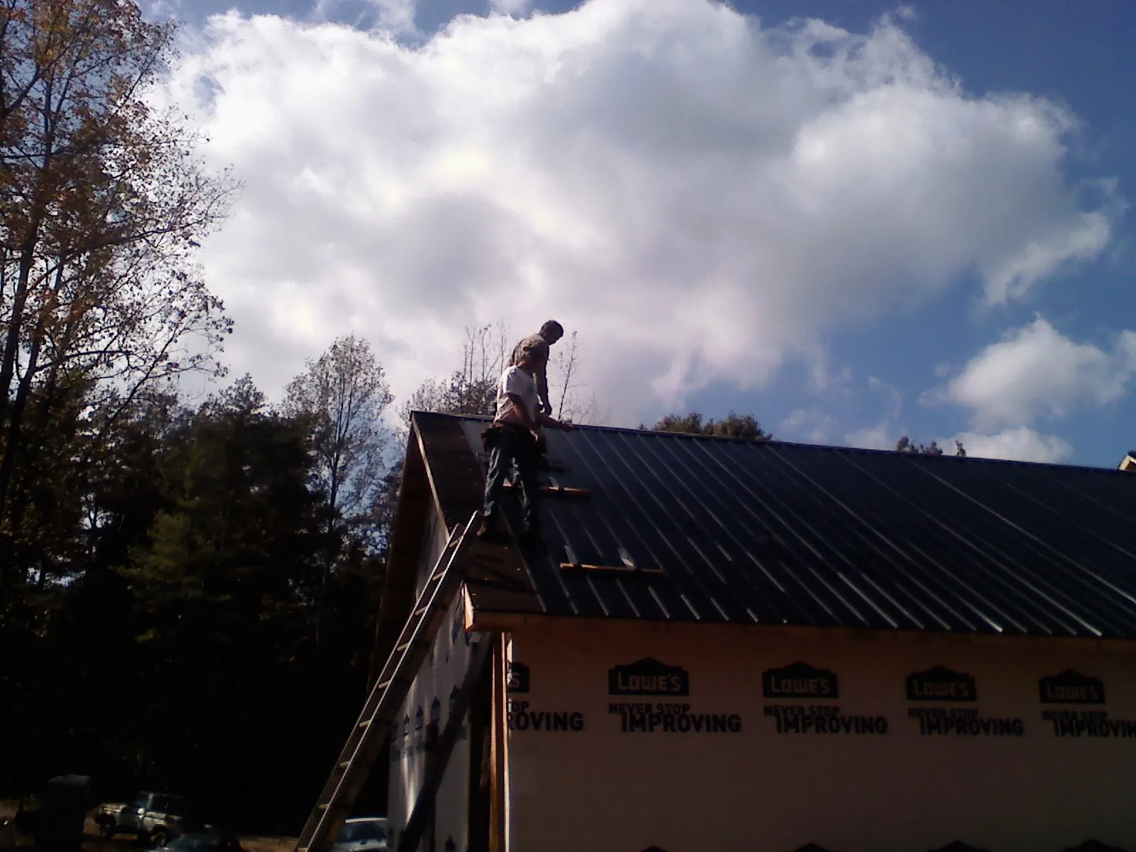Roofer fastening dark metal panels high against a cloudy sky, from a Roof Inspection job in Goose Lake