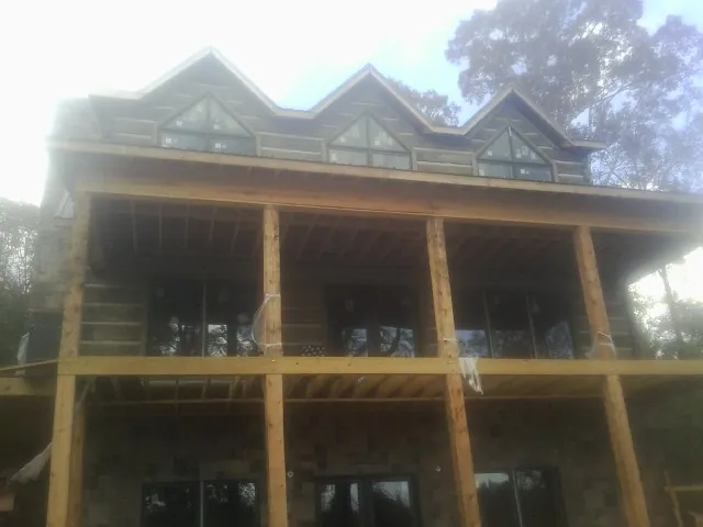 Dormers and porch framing on a large log home under construction — Roof Coating work by our crew in Goose Lake