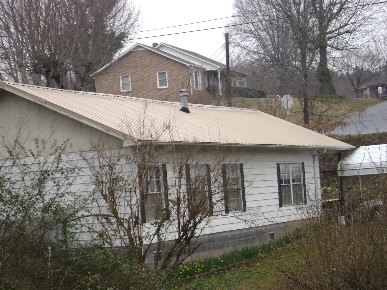 Tan metal roof on a white sided house set into a hillside — Commercial Roofing by Roofing Brothers in Goose Lake
