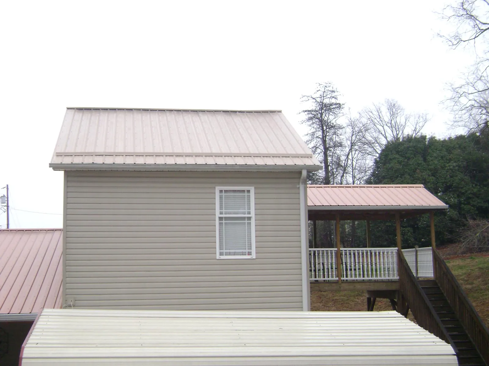 Tan metal roofs on a two story addition and attached porch, from a Roof Replacement job in Goose Lake